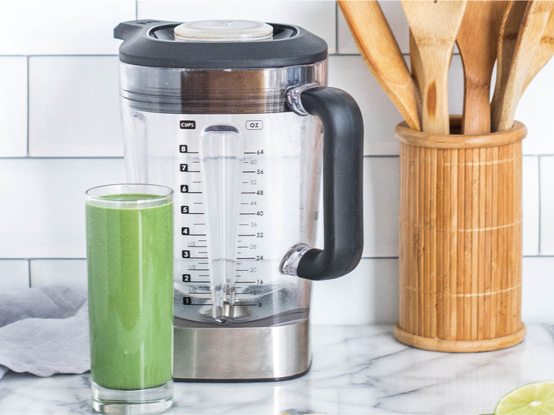 a glass of green smoothie beside a blender